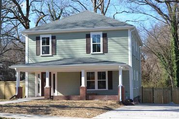 Two-story house with green siding and a front porch under a clear sky.