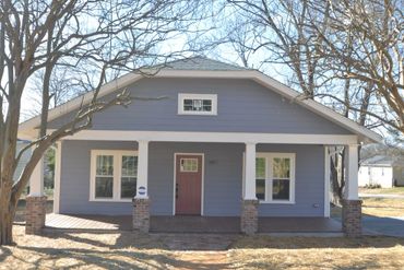 Blue single-story house with a front porch and white trim in a leafless tree setting.