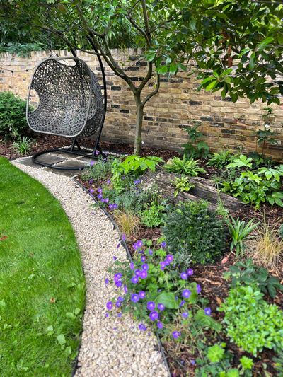 Gravel pathway between lawn and flower bed leading to a garden swing seat.