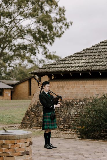 Man in traditional Scottish attire playing bagpipes outdoors.