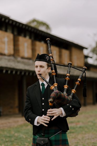 A man in traditional Scottish attire playing the bagpipes outdoors.