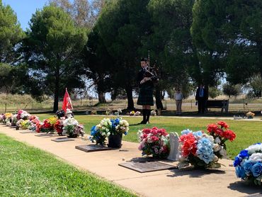 A bagpiper plays at a cemetery with colorful flowers on graves.