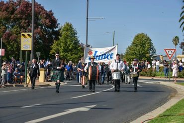 A marching band leads a parade with a 'Junee' banner on a sunny day.