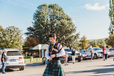A man in traditional Scottish attire playing bagpipes outdoors.