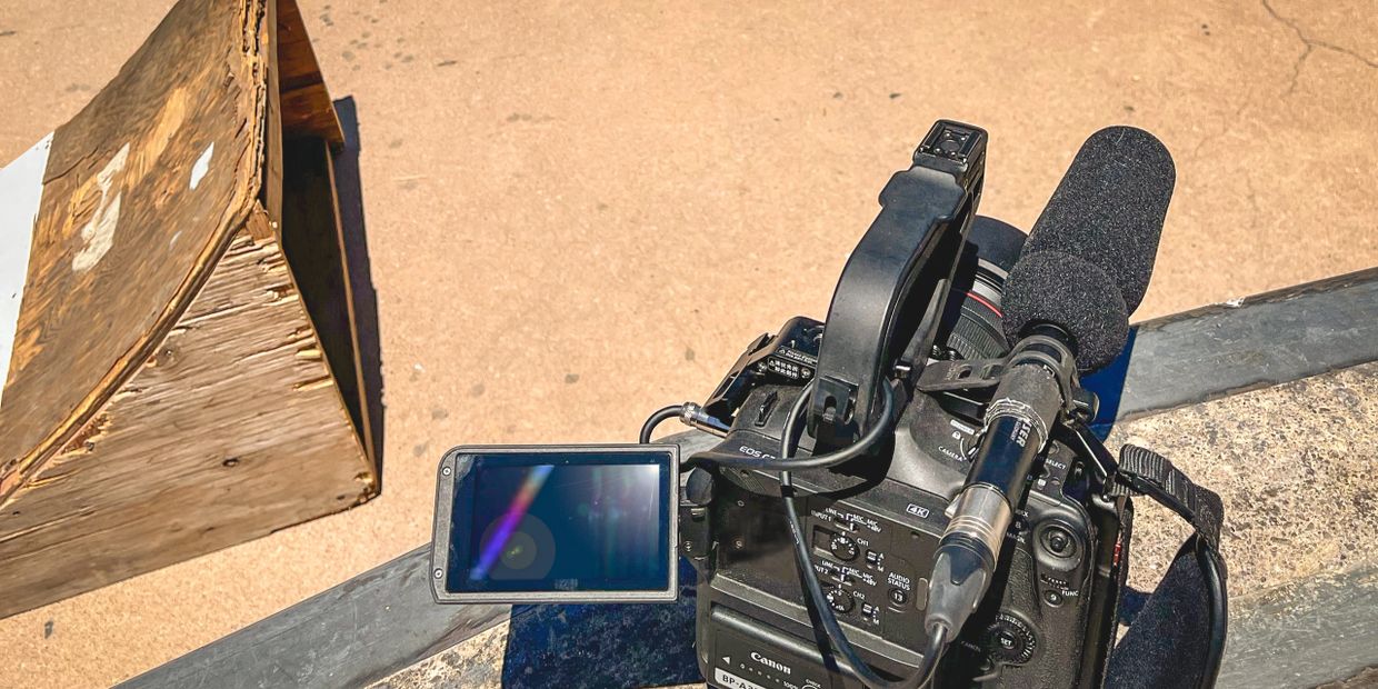 Professional Canon video camera with microphone and flip-out screen outdoors.