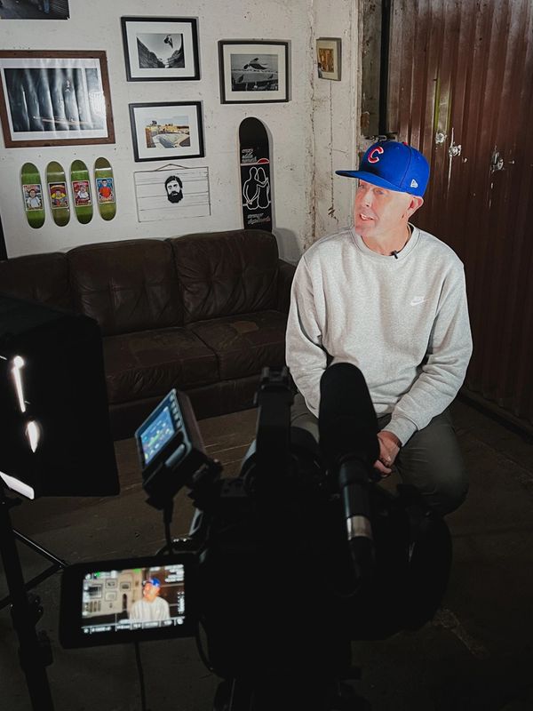Man in a blue cap being filmed in a cozy, art-decorated room.