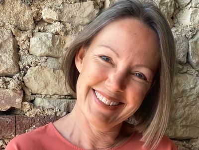 Smiling woman with short hair poses against a rustic stone wall.