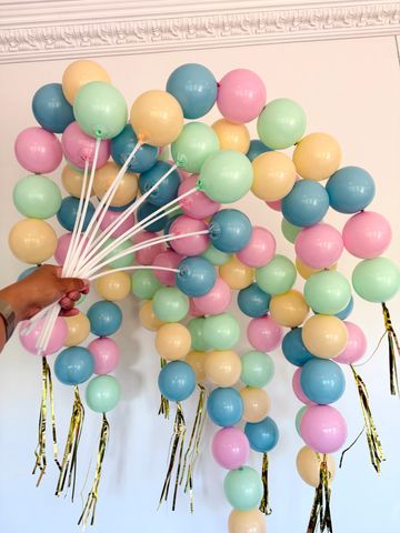 Hand holding pastel balloons with gold ribbons.