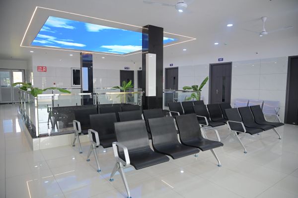 Modern waiting area with black chairs and ceiling screen showing blue sky.