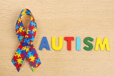 Colorful puzzle piece ribbon with the word AUTISM in multicolored letters.