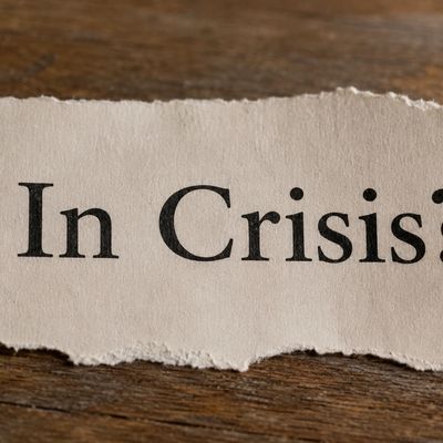 Torn paper with the words 'In Crisis' on a wooden surface.