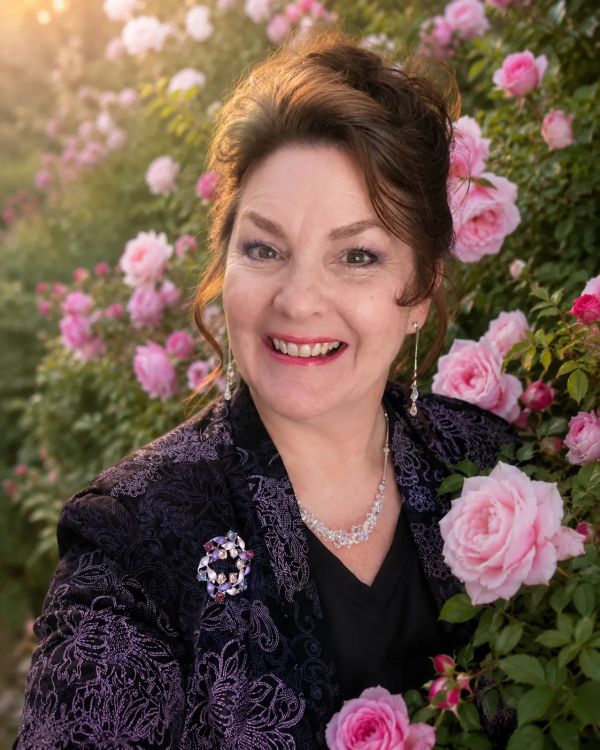 Smiling woman with pink roses in the background.