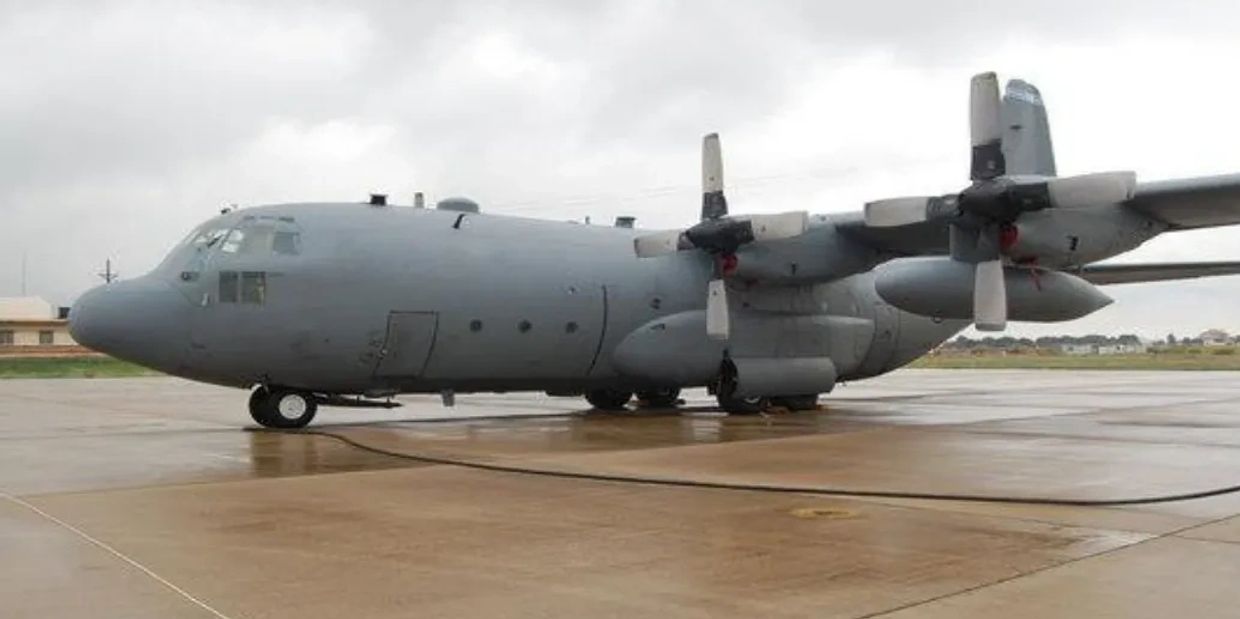 A military transport aircraft parked on a wet runway on a cloudy day.