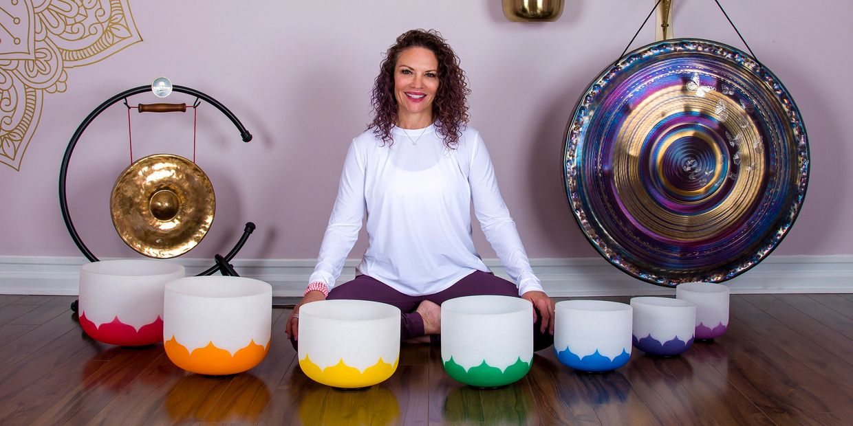 beautiful woman smiling in an array of chakra tuned crystal singing bowls and gongs
