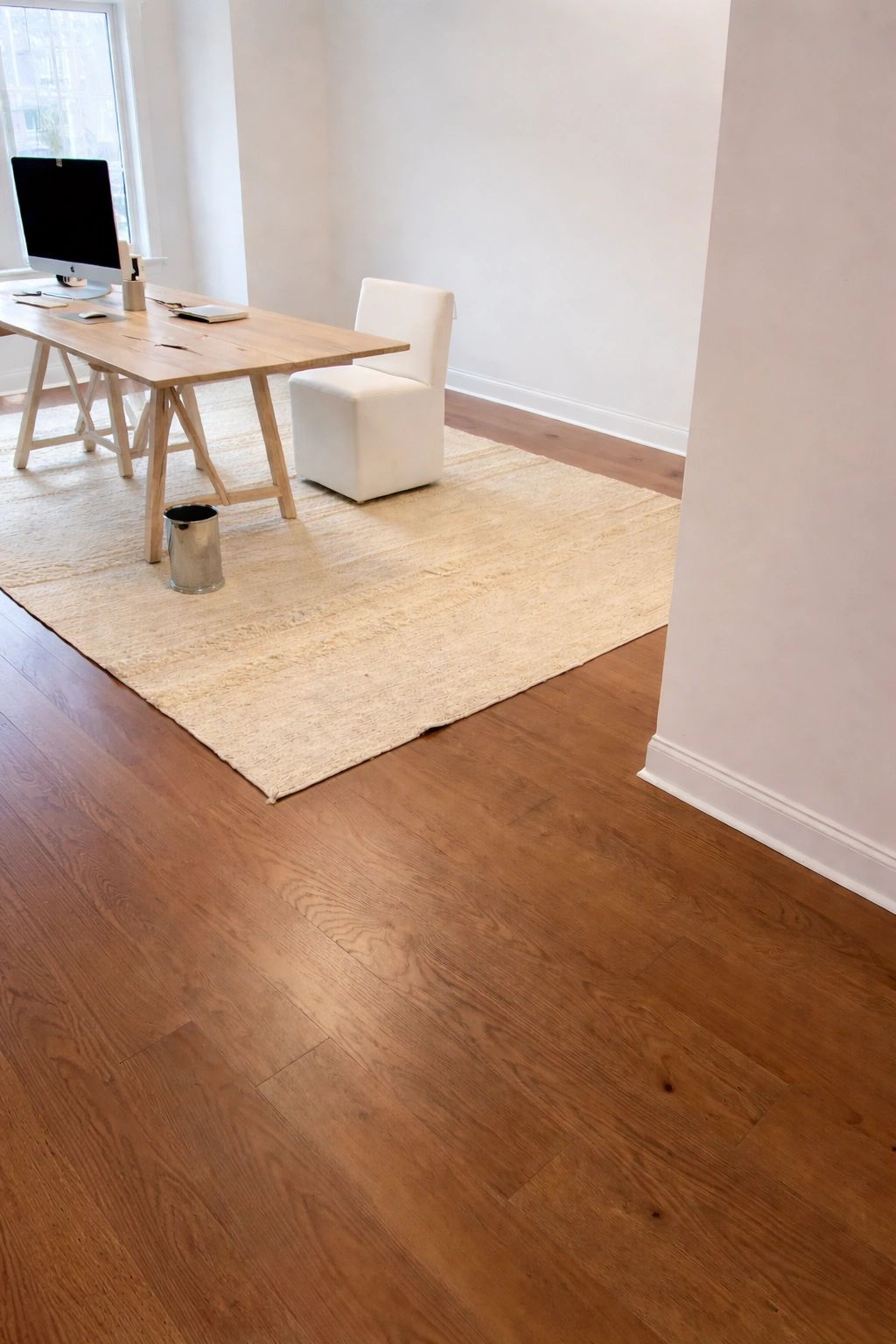 Minimalist office with wooden desk, white chair, and large window.