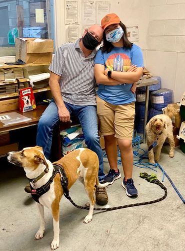 Two people with masks and two dogs in an indoor setting.