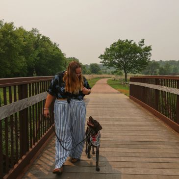 Woman walking and playing with her dog on a wooden bridge.