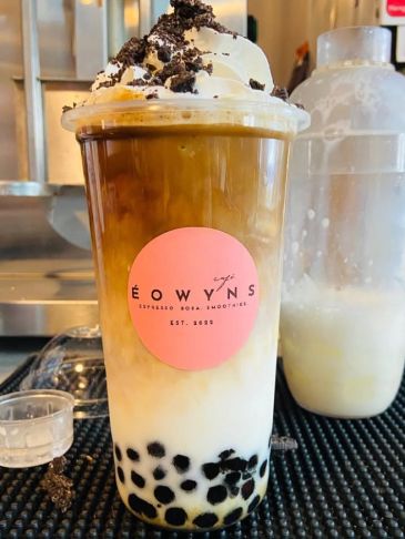 A layered iced coffee drink with boba pearls and whipped cream topped with crushed cookies.