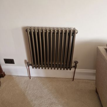 Compact metallic radiator mounted on a wall.