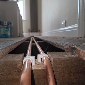 Copper pipes installed in a wooden floor underlay with exposed floorboards.