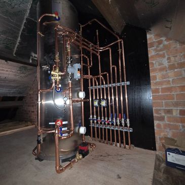 Copper pipes connected to a large tank in a basement.