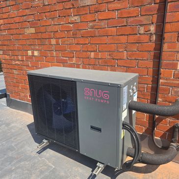 Heat pump unit installed on a rooftop against a brick wall.