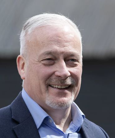 Smiling elderly man with white hair and goatee in a blue shirt and jacket.