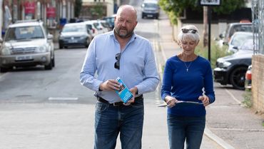 A man and woman walk down a street holding papers and pens.