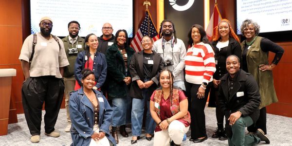 A diverse group poses happily in a conference room with American flags.