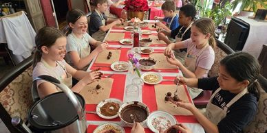 Children making chocolate treats together around a festive table.