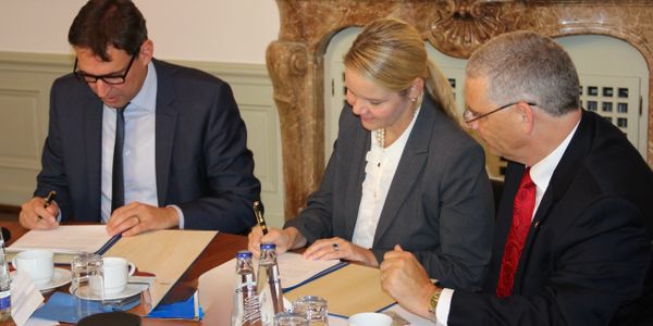Three professionals signing documents at a formal meeting.