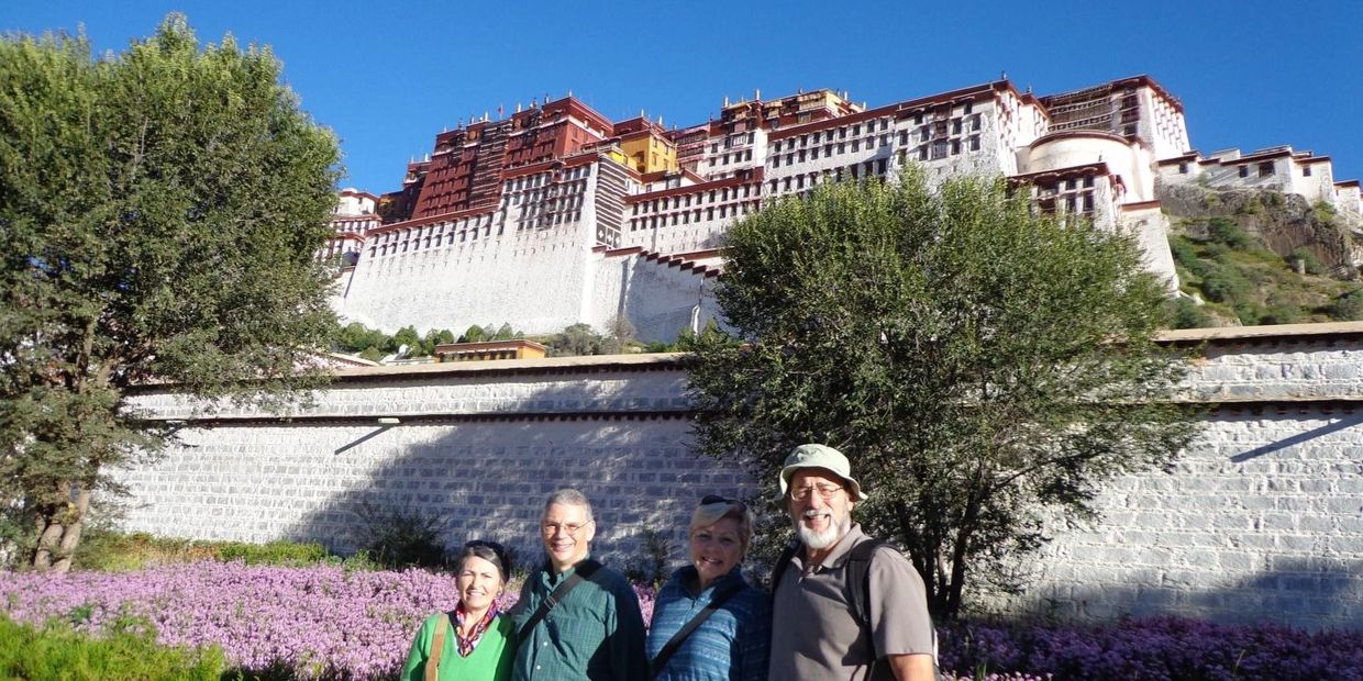 Four tourists posing with the Potala Palace in Tibet behind them on a sunny day.