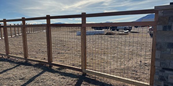 Wooden and wire fence enclosing a dry field under a blue sky.