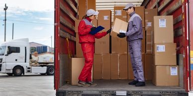 Two delivery workers handling and checking packages inside a truck.
