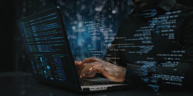 Person typing code on laptop with digital code overlay in dark setting.