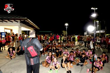 Coach addresses young soccer players and supporters at a night event.