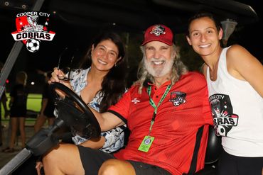 Three smiling people in Cooper City Cobras gear pose in a golf cart.