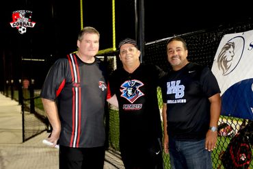 Three men posing together at a nighttime sports field event.