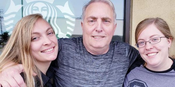 Three people smiling in front of a Starbucks window.