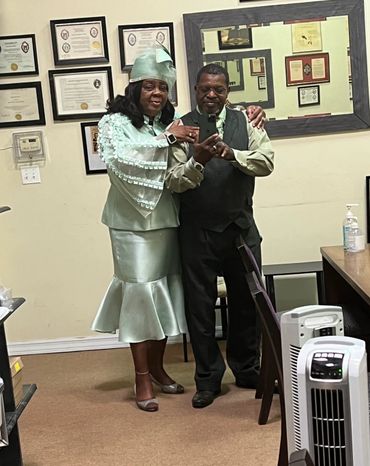 A couple dressed elegantly, posing for a mirror selfie in an office room.