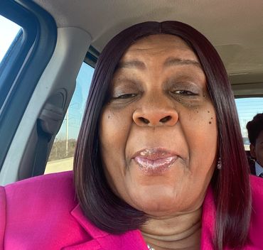 Woman in pink blazer taking a selfie inside a car.