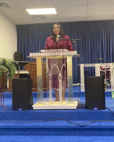 Woman speaking at a church podium with blue curtains.