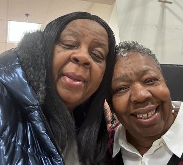 Two elderly women smiling closely together in a warm indoor setting.
