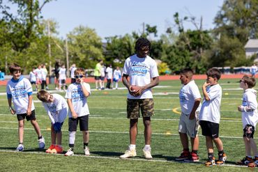 Kids in a sports camp lined up on a field with a coach giving instructions.