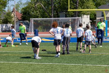 Children warming up on a football field with coaches during practice.