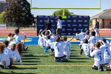 Children on a football field following instructions during an outdoor event.