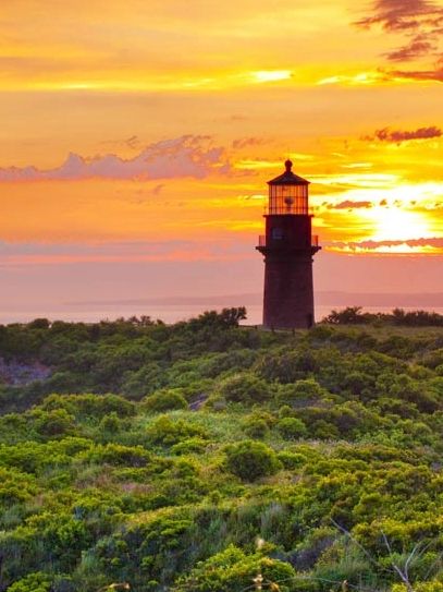 A lighthouse on a green hill during a vibrant sunset.