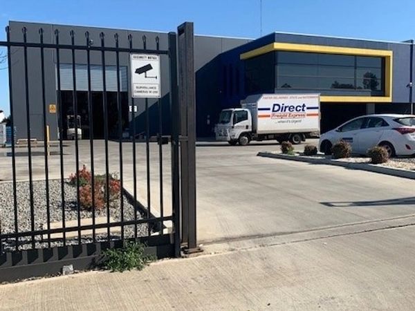Industrial building with a delivery truck and security gate on a clear day.