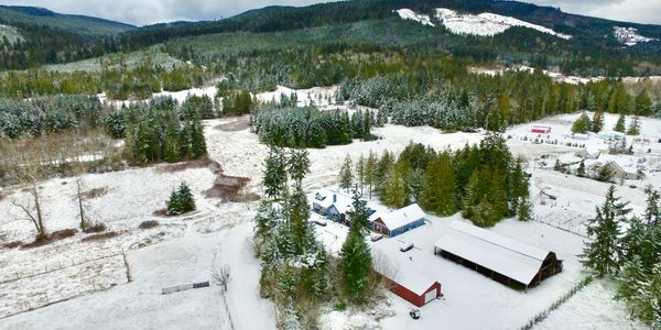 Snow-covered rural landscape with farm buildings and forested hills.