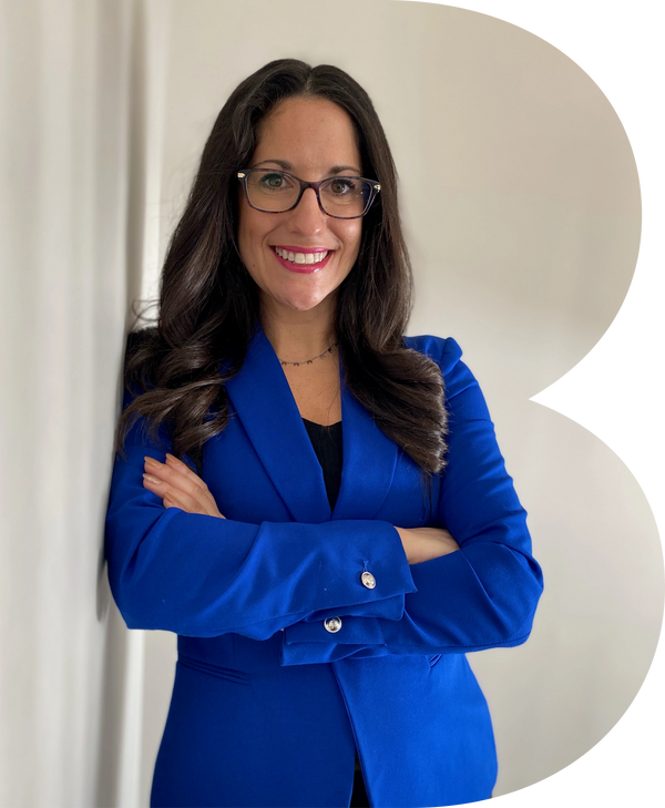 A woman in a blue blazer and glasses looking at camera, smiling with arms crossed.